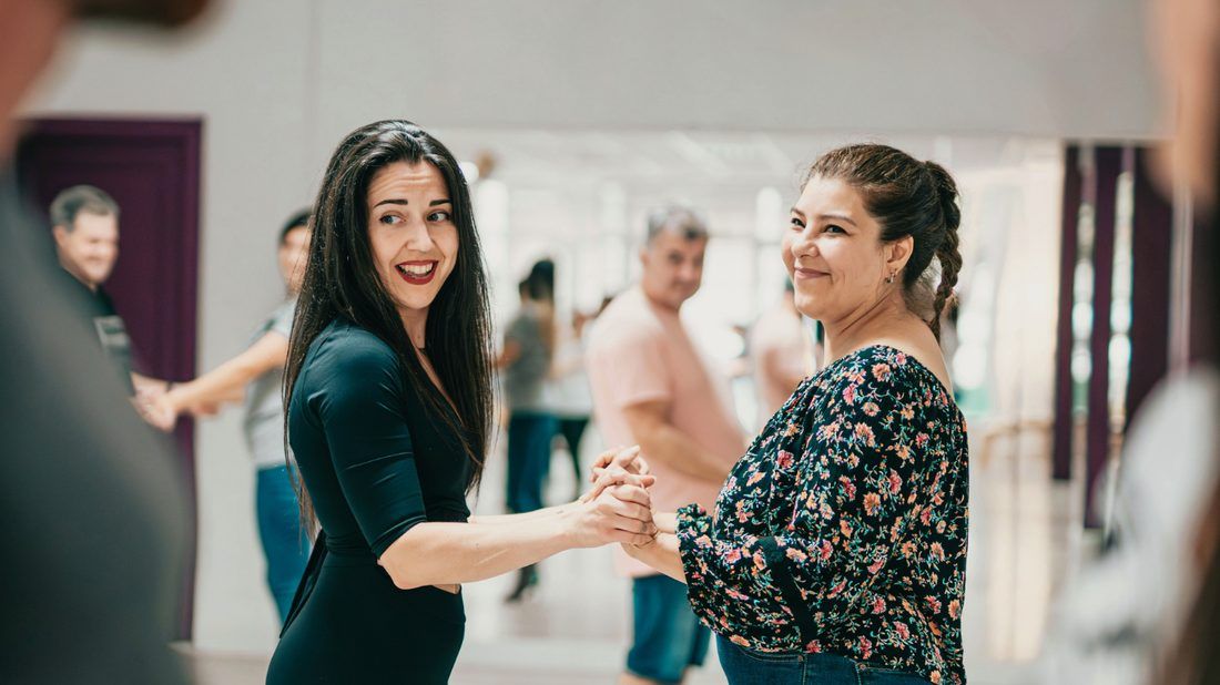 Twee danspartners houden elkaars hand vast en lachen tijdens de les